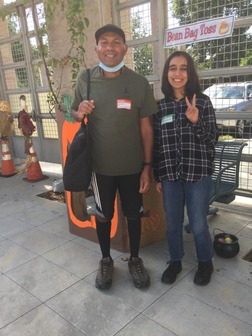 man and woman stand smiling outside with pumpkin behind them