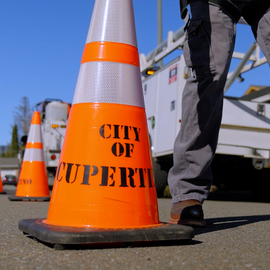 Traffic cone with City of Cupertino lettering in foreground and maintenance vehicle in background