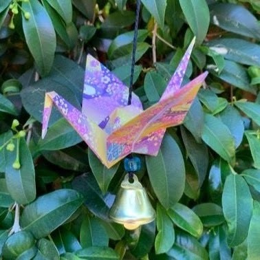 Paper crane with bell attached. Bush in background