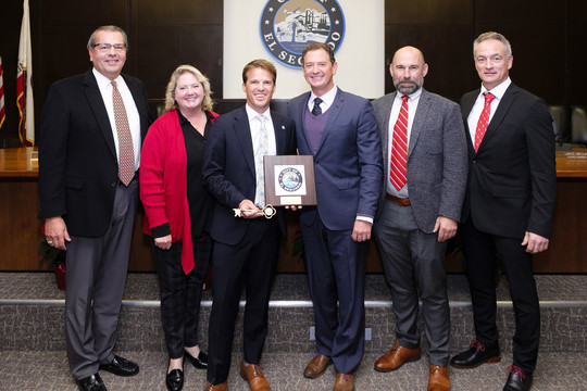 Councilmember Scot Nicol holding a plaque and key to the city with City Councilmembers and City Manager in council chambers.