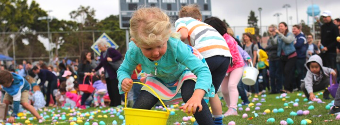 Little girl picking up egg in grass at egg hunt