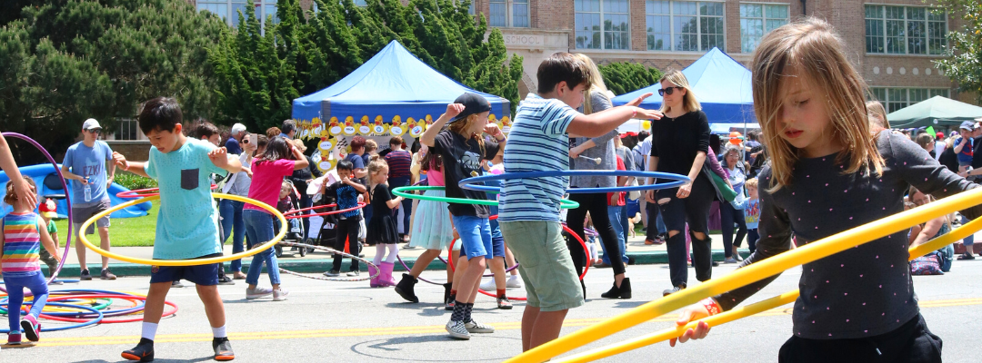 Kids hula hooping with booths, bounce houses, and crowds in the background