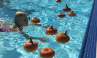 Girl in pool swimming with pumpkins
