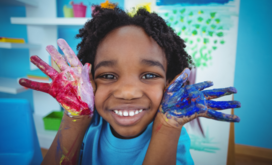 young kid smiling with hands covered in paint