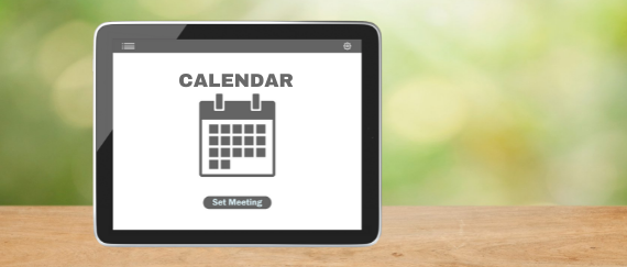calendar icon on tablet sitting on wood and green background 