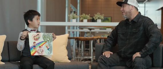 student holding artwork and talking to male series host