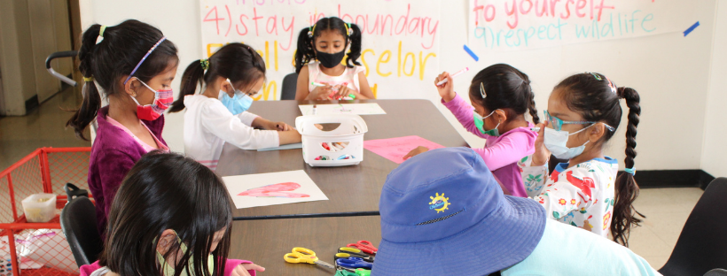 children in masks coloring at a table