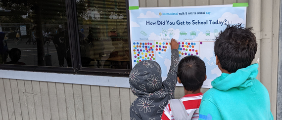 three students putting up dots on sign for how they got to school: walking, rolling, carpool, bus or transit