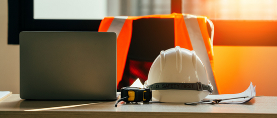 office with laptop on desk, hardhat, and safety vest