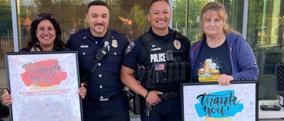 police officer and firefighter standing with Fremont Chamber of Commerce members holding framed Thank you posters.