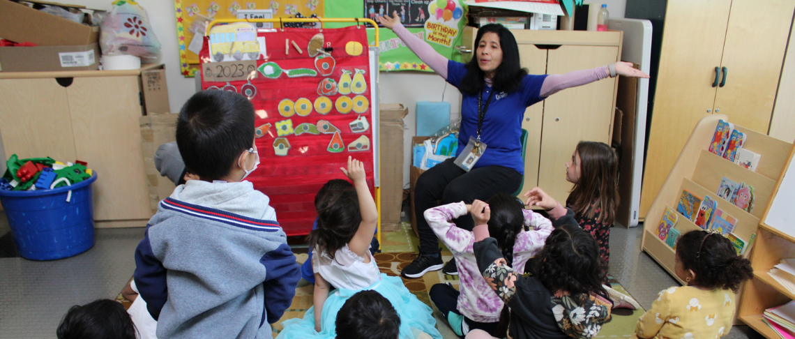 Tiny Tots teacher with students in the classroom sitting on the floor on rug