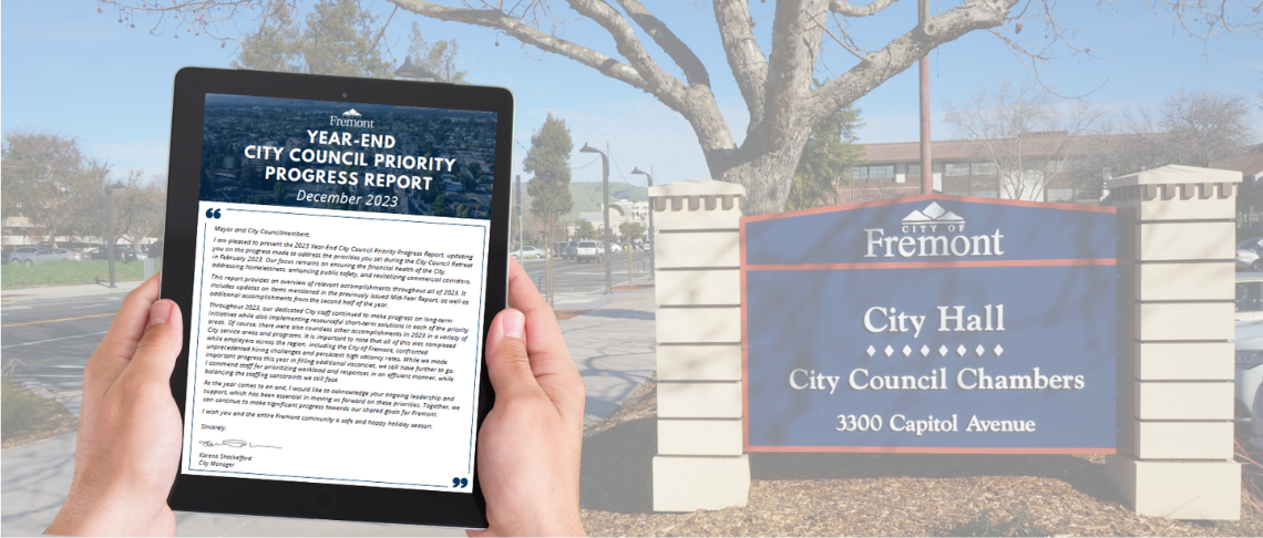 person holding tablet with Council Priorities Report on screen. City Hall sign in background