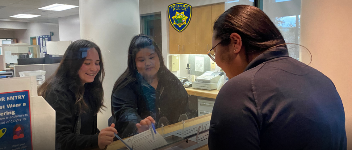 two employees from the Fremont Police Department helping a customer at the counter in the department lobby 