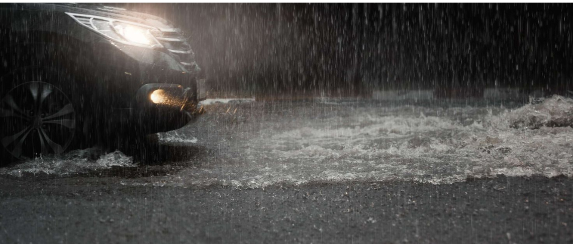 car with headlights on driving in the rain with puddles on roadway