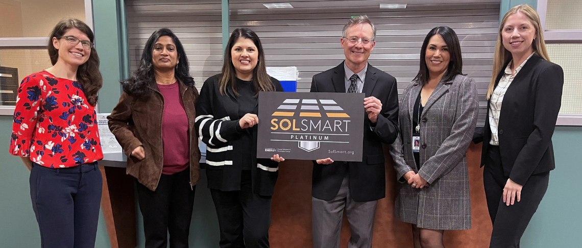 City staff holding SolSmart Platinum Designation signage in City Hall lobby.