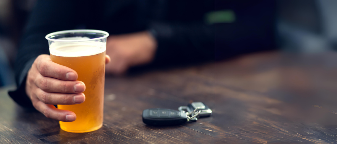 person holding a beer with car keys on table