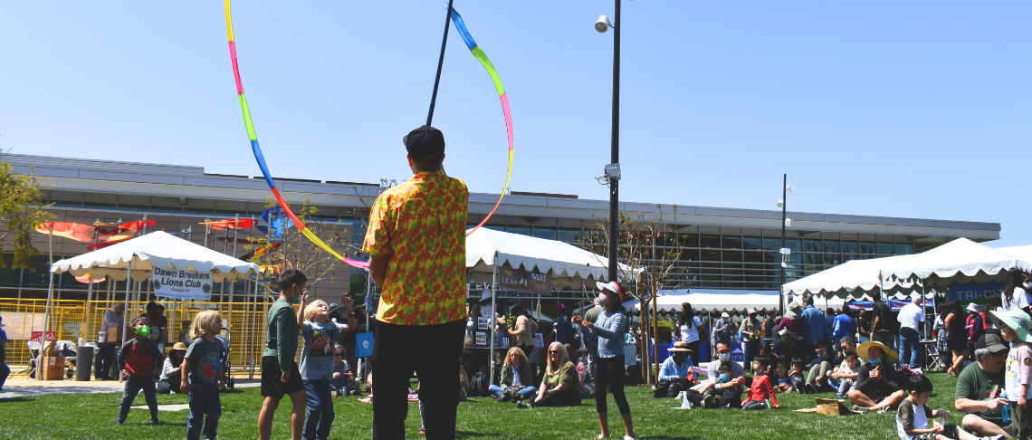 Earth Day Fair with event attendees sitting on the grassy knoll watching a person with a kite