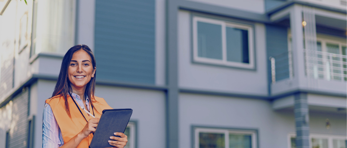 inspector in orange vest holding clipboard with apartments in background