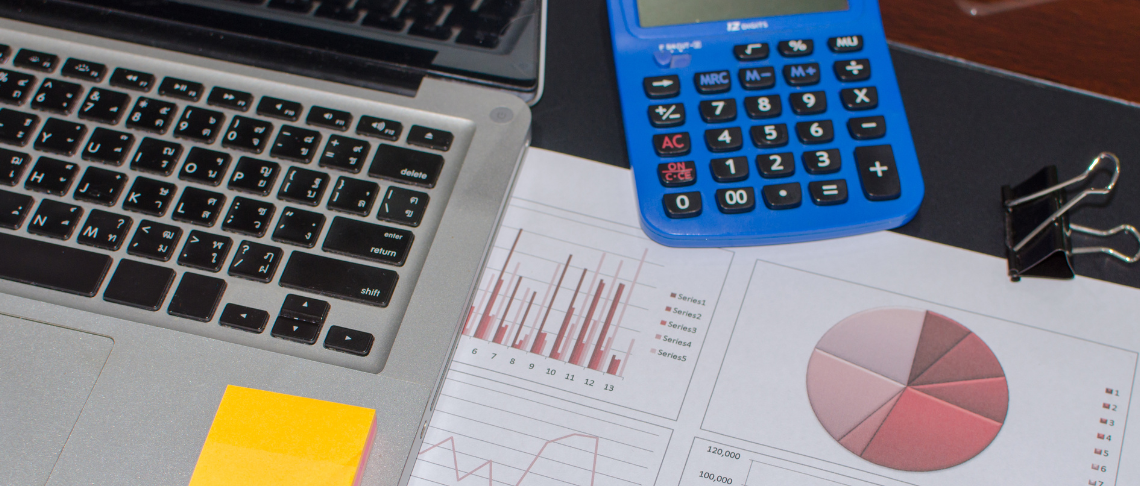 A financial document on a table with a pen, calculator, coins, and glasses laying on top of it. 