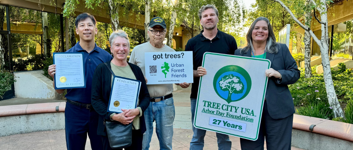 City staff and volunteers from Friends of Urban Forestry holding Tree City USA for 27 Years sign, proclamations, and other tree-related posters
