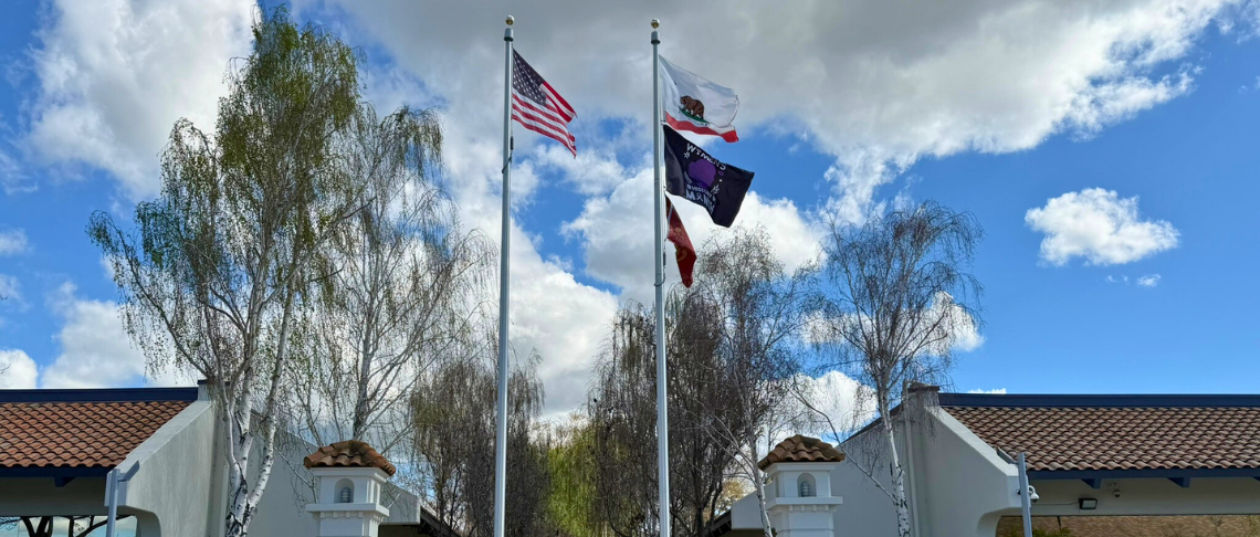 Four flags on flagpoles at City Hall under a partly cloudy sky.   