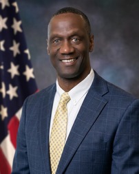 Fremont Police Chief Floyd Mitchell in blude suit and yellow patterned tie posing in front of an American flag backdrop.