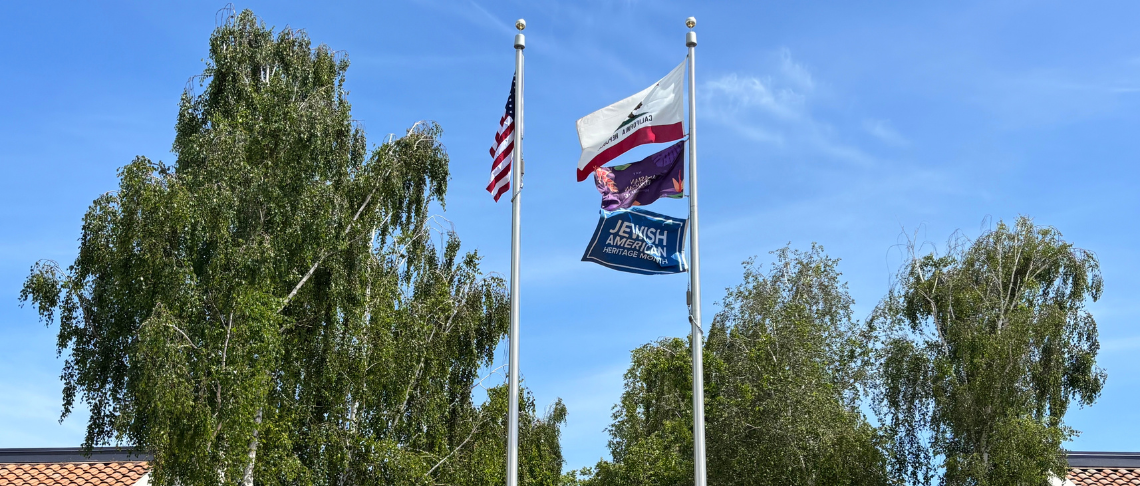four flags on flagpole at City Hall with blue sky and clouds in background