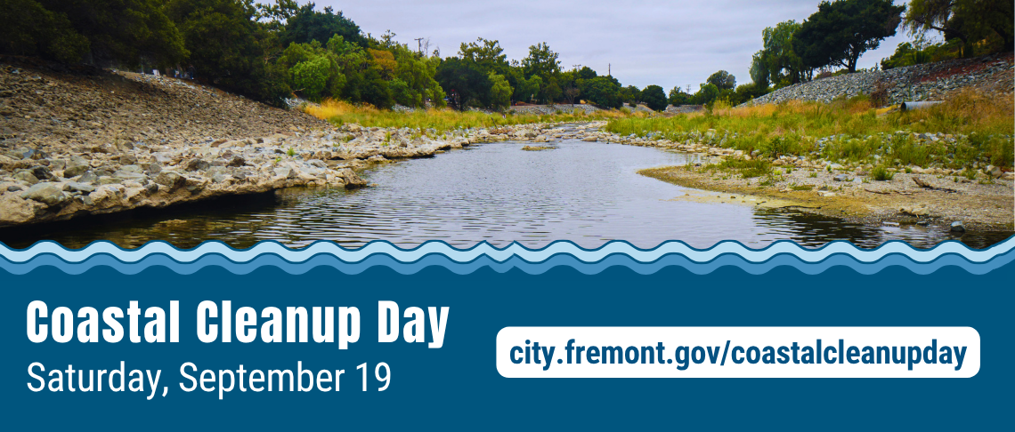 Shallow river flowing through rocky banks with green trees under a cloudy sky, promoting Coastal Cleanup Day on September 19.