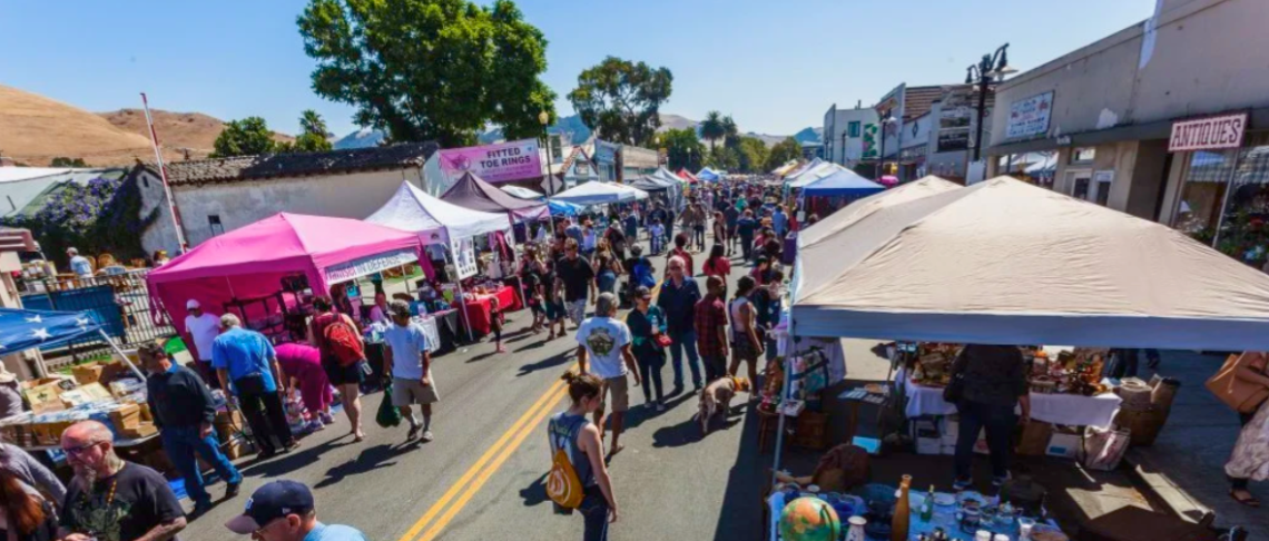 Crowded outdoor market with colorful tents and people browsing stalls on a sunny day.
