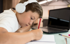A child wearing headphones doing homework with a red pen