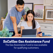 A couple sitting at a table looking at their laptop. Text" SoCal Gas Assistance Fund now available to qualifying customers." 