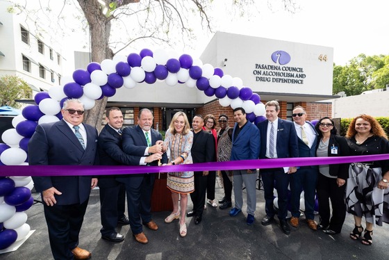Supervisor Kathryn Barger stands behind a purple ribbon and in front of an archway of white and blue balloons, with a group of people around her ready to do a ribbon cutting
