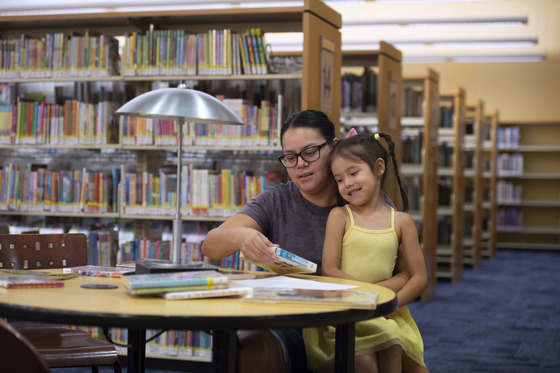 Mother and daughter sitting a table full of books at library