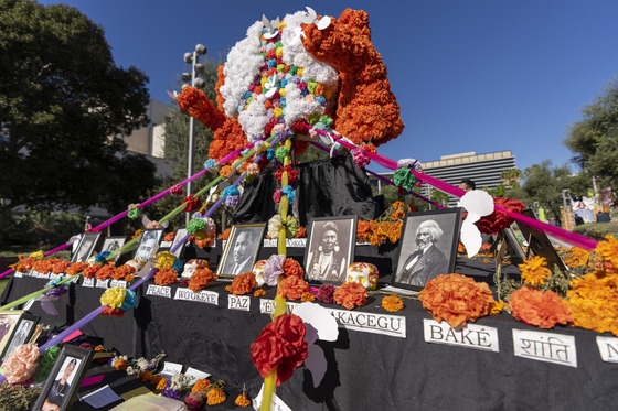 Community altar with images of loved ones, and famous figures who have passed away with orange flowers next to images at Gloria Molina Grand Park