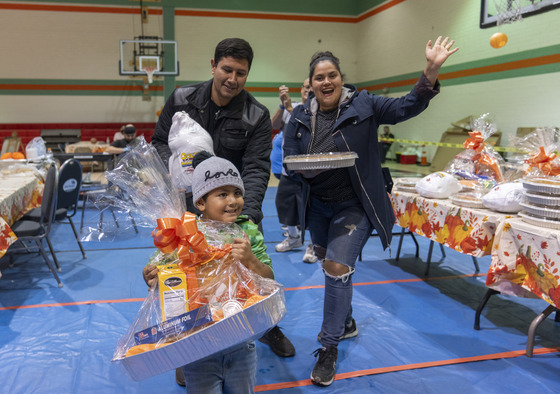 Boy with beenie holding a tray with food gift and a male and female behind him holding a pie smiling at Bassett Park