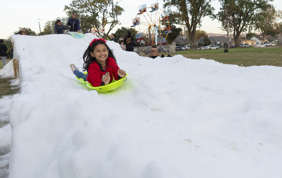 Girl in red shirt on her belly doing down a sled on snow at Sorensen Park in Whittier