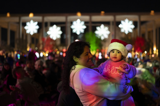 Woman holding girl in her arms with crowd behind them at LA County Tree Lighting Ceremony in downtown Los Angeles