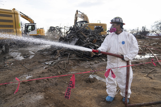 Army Corps of Engineer man with white jumpsuit, helmet, goggles, face mask is holding a water hose as he sprays debris