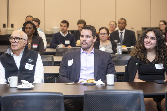 Male and females dressed professionally are seating at tables that are in rows