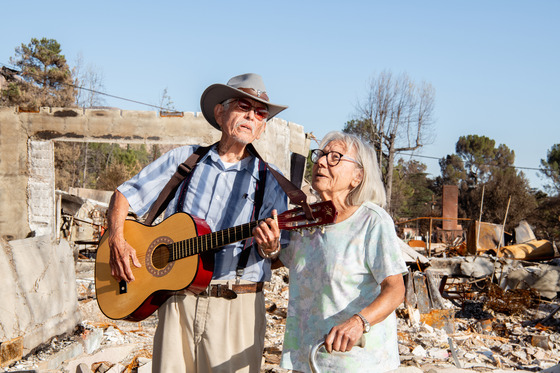 Older couple sing in front of debris from the site of their home in Altadena