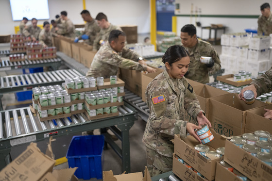 Men and women in the National Guard in an assembly line placing cans of food in boxes