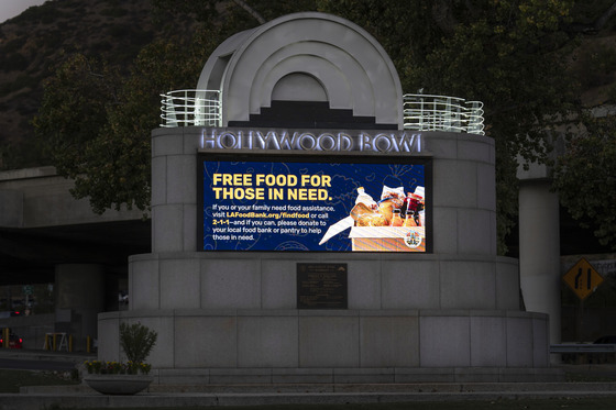 Hollywood Bowl entrance with food assistance sign with street sign, trees, and bridge in the background during sunset