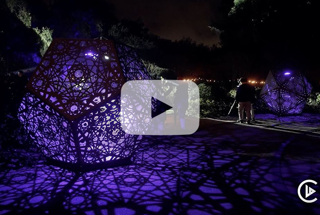 Dazzling geometric sculptures with purple shining through them and people next to sculptures at night