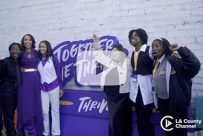 Group of women standing next to each other in front of purple and white signage that says Together We Thrive