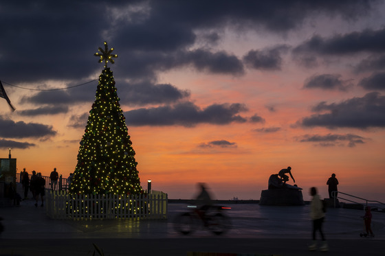 Christmas street with lights at the beach with people, skateboarders, and bicyclist during a sunset with clouds