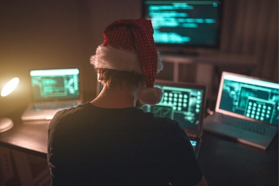 The back of mans head who is wearing a red Santa hat and is in front of laptops and monitors