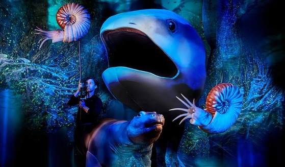 Man holding Ammonite on stick, another Ammonite floating, shark, and Desmostylian puppets