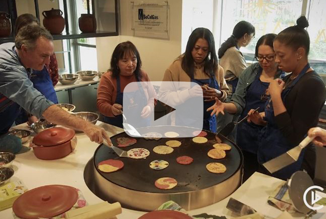 Men and women standing next to griddle where they are warming up tortillas