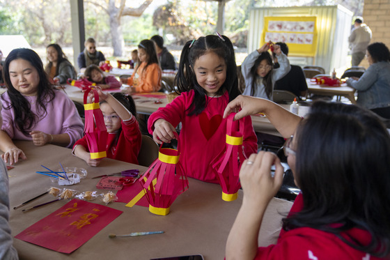 Girls holding hand made red and yellow Chinese lanterns on table with other children sitting at tables around them