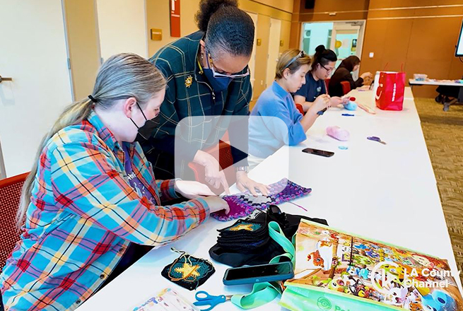 Row of people sitting at a table in room and crocheting 